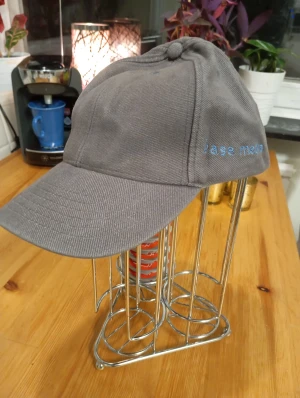 Grå keps med blå text - Snygg grå keps med böjd skärm och broderad blå text 'jase mean' på sidan. Kepsen har klassisk form med knapp på toppen och är tillverkad i ett slitstarkt bomullsmaterial. Perfekt för dig som vill ha en enkel och stilren look.