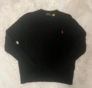 Ralph Lauren tröja - Superfin och klassisk kabelstickad tröja i Svart. Mjuk, varm och sitter snyggt. Perfekt för både vardag och lite finare tillfällen.  ✔ Äkta Polo Ralph Lauren ✔ Ikoniska ryttaremblemet ✔ Bra skick – inga fläckar eller hål  Storlek:S Passform: Normal Färg: Svart 