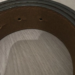 Svart och brunt skärp i skinn - Snyggt svart och brunt bälte i skinn med klassisk design. Bältet har flera hål för justering och en stilren look som passar till jeans eller kostymbyxor. Perfekt accessoar för att lyfta din outfit.