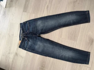 Mörkblå jeansbyxor George, storlek 31 - Snygga mörkblå jeansbyxor från George i klassisk femficksmodell. Jeansen har kontrastsömmar och lätt slitna detaljer framtill och baktill för en cool look. Passformen är rak med normal midja och materialet är robust denim.