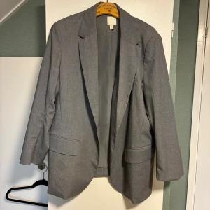 Grå kavaj från H&M, storlek XL - Snygg grå kavaj från H&M i storlek XL. Klassisk modell med två framfickor och smal krage. Kavajen har en stilren, rak passform och är tillverkad i ett mjukt, lätt material med slät insida. Snygg att ha som jacka/för att bli lite mer uppklädd på en utekväll 🌟