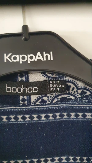 Klänning - Säljer en blåvit klänning från Boohoo med unikt orientaliskt mönster. Klänningen har lång ärm och är lätt och flowy i modellen. Den har öppen front utan knappar och ger en chill vibe till din outfit.