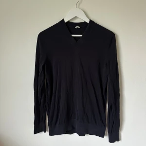 Mörkblå v-ringad tröja från Arket - Mörkblå v-ringad tröja från Arket i storlek S. Tillverkad i en mjuk mix av bomull och silke som känns skön mot huden. Tröjan har lång ärm, ribbade muddar och klassisk passform. Perfekt för dig som gillar stilrena och enkla plagg. 4Ö20