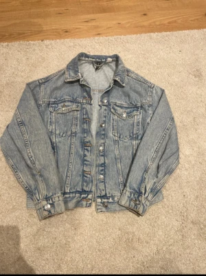 Blå jeansjacka från Divided XXS - Säljer en klassisk blå jeansjacka från Divided i storlek XXS. Jackan har snygga knappar framtill, två bröstfickor med lock och krage. Perfekt för dig som gillar en tidlös och chill stil. Passar dig som vill ha en jacka med normal passform och cool denim-look.