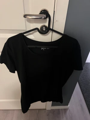 Svart t-shirt från You XL - En enkel svart t-shirt från You i storlek XL. Modellen har rund halsringning och korta ärmar, perfekt för en clean och stilren look. Materialet känns mjukt och bekvämt mot huden. Passar dig som gillar basic och minimalistisk stil.