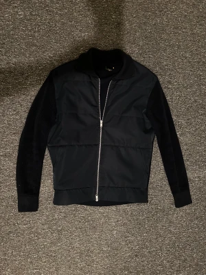 Mörkblå cardigan från Massimo Dutti - Blå cardigan från Massimo Dutti med stickade ärmar och krage, samt quiltad front i syntetmaterial. Jackan har hel dragkedja och en clean, modern look. Perfekt för dig som gillar stilrena plagg med lite edge. Passar dig som vill ha en jacka med både komfort och snygg design. Väldigt fett och knappt använd💯S/M i storlek