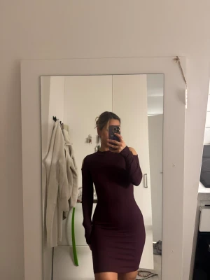 Vinröd ribbad kortklänning med cut-outs - Säljer en vinröd, ribbad kortklänning med lång ärm och snygga cut-outs vid axlarna. Klänningen har en tight passform och är tillverkad i ett stretchigt material som sitter skönt mot kroppen. Perfekt för dig som gillar stilrena detaljer och vill sticka ut.