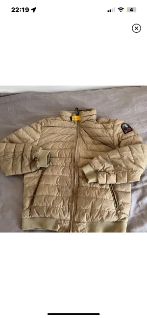  pufferjacka  Parajumpers - Snygg beige pufferjacka från Parajumpers med broderad patch på ärmen och gul detalj vid kragen. Jackan har ribbade muddar, dragkedja framtill och två sidofickor med zip. Perfekt för dig som vill ha en clean och stilren look under kyliga dagar. Såklart Äkta sällsynt färg på just den modellen pris kan diskuteras 