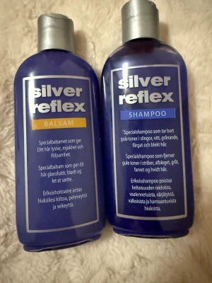 Silver Reflex balsam och schampo - Två flaskor Silver Reflex, ett balsam och ett schampo, båda i lila plastflaskor med silverfärgade lock. Balsamet ger glans och mjukhet, schampot tar bort gula toner i blont, grått och färgat hår. Varje flaska innehåller 200 ml och har tydlig etikett på framsidan.