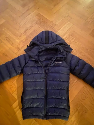Mörkblå Peak Performance dunjacka - Säljer en snygg mörkblå jacka från Peak Performance, jackan hade ett litet hål på baksidan men det är nu fixat med en läderlapp. Annars är den i gott skick och redo att säljas. Öppen för byte🤗
