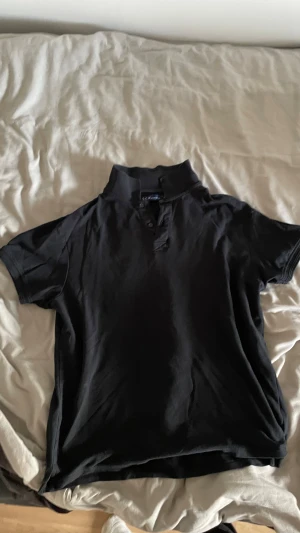 Svart kortärmad henley från S.Oliver - Svart henley från S.Oliver med korta ärmar och klassisk krage. Skjortan har knappar vid halsen och är gjord i mjuk bomull som känns skön mot huden. Perfekt för dig som gillar enkel och stilren design.