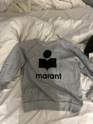 Grå sweatshirt från Isabel Marant Étoile - Snygg grå sweatshirt från Isabel Marant Étoile med stort svart logotryck på bröstet. Tröjan har rund hals, ribbade muddar och är tillverkad i mjuk bomullsmix. Perfekt för en chill och trendig look. Skulle säga att den sitter som S❤️ Pris kan diskuteras