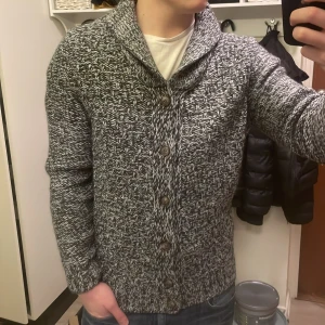 Grå stickad cardigan - Otroligt fet vit grå stickad cardigan i toppskick. Perfekt nu till kallare väder. Modellen är 180cm, 74kg. Priset kan diskuteras!