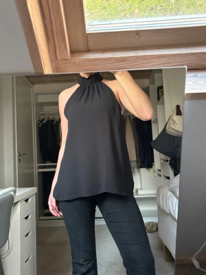 Svart Blus  - Säljer en svart blus från H&M i storlek XS. Toppen har en hög krage med volangdetalj och är ärmlös med en loose passform. Materialet är lätt och flowy, perfekt för att skapa en chill och stilren look. Passar dig som gillar minimalistisk stil. Aldrig använd🩷🩷