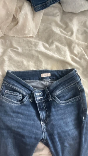 Blå bootcut jeans från Nelly - Snygga blå bootcut jeans från Nelly med klassisk femficksdesign och kontraststickningar. Bakfickorna har vit broderad dekor som ger extra attityd.