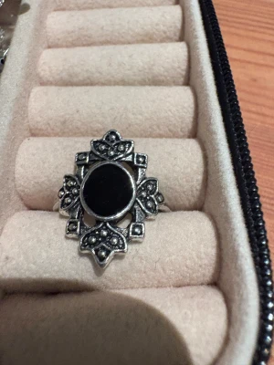 Vintageinspirerad silverring med svart sten - Unik ring i silverfärgad metall med en rund svart sten i mitten. Ringen har detaljerad, ornamenterad ram med små prickar och blommiga former som ger en cool vintagekänsla. Perfekt för dig som gillar statement-smycken med lite edge.