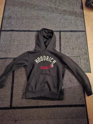 Svart hoodie från Hoodrich med tryck - Svart hoodie från Hoodrich med stor vit logga och texten 'From Nothing To Something' framtill samt 'product of the streets' i stor stil på ryggen. 