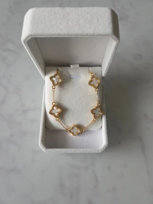 Armband  - Ett elegant armband med vita klöverdetaljer. Perfekt för att komplettera din stil.