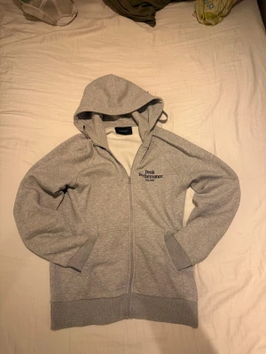 Peak performance  - Grå peak performance zip hoddie i storlek M. Hoddien har två fickor framtill, en luva med snörning. Tröjan har även broderat den klassiska loggan på vänster bröst.