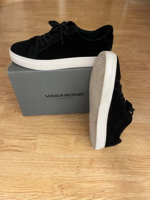  Vagabond skor - Snygga svarta sneakers från Vagabond med ovandel i mjuk mocka och vita platta sulor. Skorna har rund tå, svarta snören och en stilren design som passar till jeans eller dressade outfits. Den ända defekten på skorna ser man på bild 6, sko boxen medföljer även😊pris ej hugget i sten😏också använda fåtal gånger i somras.