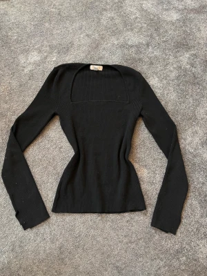 Svart ribbad långärmad topp - Säljer en svart ribbad topp med lång ärm och fyrkantig halsringning. Modellen är slim och sitter snyggt figurnära. Perfekt för dig som gillar minimalistisk stil och vill ha en enkel men trendig topp i garderoben.