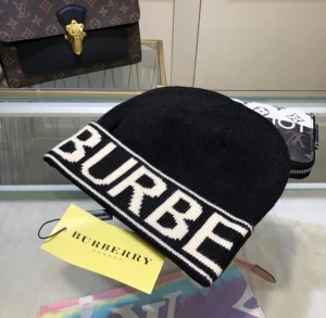 Svart Burberry mössa med logga - Snygg svart stickad mössa från Burberry med stor vit logotyp runt kanten. Mjuk och skön passform, perfekt för kalla dagar. Klassisk design med kontrastfärgade detaljer som ger en cool vibe.