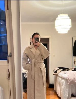 Beige kappa från NA-KD med bälte - Lång beige kappa från NA-KD knytskärp i midjan. Rak passform och långa ärmar. Rätt tung och tjock i tyget. Använd enstaka gånger