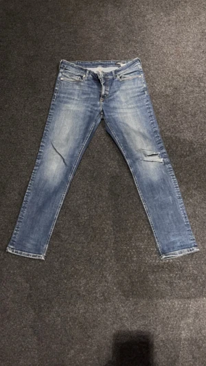 Blå jeans med slitningar och raka ben - Snygga blå jeans med slitningar på ena benet och klassisk femficksdesign. Jeansen har en rak passform och är tillverkade i jeansmaterial med ljus tvätt. Perfekt för dig som gillar en avslappnad och trendig look.