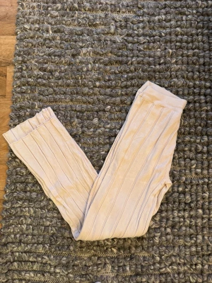 Ribbstickade vit byxor från Stories - Säljer ett par ribbstickade vit byxor från Stories i storlek L. Byxorna har en mjuk, stickad känsla och elastisk midja för extra komfort. De är raka i modellen och har ett snyggt ribbat mönster som ger en cool vibe.