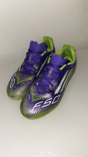 Adidas F50 lila/gula fotbollsskor - Säljer ett par Adidas F50 fotbollsskor i en riktigt fet lila och gul färgkombo. Skorna har snörning, mönstrad ovandel och klassiska dobbar för gräsplan. Perfekta för dig som vill sticka ut på planen och få max speed. Märkta med F50 och Adidas-logga på hälen.