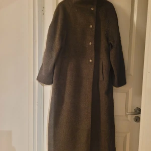 Mörkbrun kappa från Nelly med bälte - Säljer en lång och snygg mörkbrun kappa från Nelly i storlek M. Kappan har bred krage, knappar framtill, fickor på sidorna och ett matchande bälte i midjan. Materialet är ullblandning som ger en mjuk och varm känsla. Perfekt för höst och vinter. Använd endast 1 vecka. Nypris 999:-