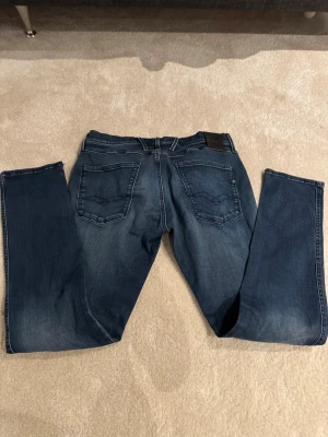 Replay Hyperflex Anbass jeans blå.   W-33 L-32.       3 - Snygga Replay Hyperflex Anbass jeans i mörkblå tvätt med klassiska fem fickor och diskreta slitningar. Stretchigt material för skön passform och smal siluett. Dragkedja och knapp framtill, samt Replay-logga på bakfickan.