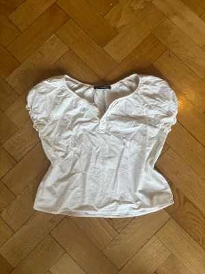 Vit blus från Brandy Melville - Säljer en söt vit blus från Brandy Melville med puffiga korta ärmar och knappar framtill. Blusen har en rundad halsringning och är gjord i mjuk bomull. Perfekt för en chill sommardag, med fina rynkdetaljer vid axlarna och ärmsluten.