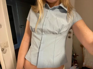 Ljusblå kortärmad skjorta med knappar - Snygg ljusblå skjorta med korta ärmar och markerad midja. 