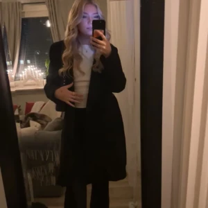 Svart kappa med bälte från Bik Bok - Säljer en svart ullblandad kappa från Bik Bok i storlek S. Den har ett snyggt bälte i midjan och klassisk krage. Kappan är långärmad och har en stilren, enkel design som är lätt att matcha med olika outfits. Perfekt för dig som gillar minimalistisk stil.