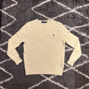 Polo Ralph Lauren tröja - Säljer en klassisk stickad tröja från Polo Ralph Lauren i beige med blå broderad logga. Tröjan är aldrig använd bara testad, tröjan är storlek S men passar som M hör av er vid minsta funderingar!