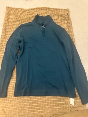 Blå half zip tröja Christian Berg - Snygg blå långärmad tröja från Christian Berg Premium Edition i ekologisk bomull. Tröjan har en hög krage och half zip-dragkedja framtill, perfekt för en chill och stilren look. Passar dig som gillar enkel design med lite edge.