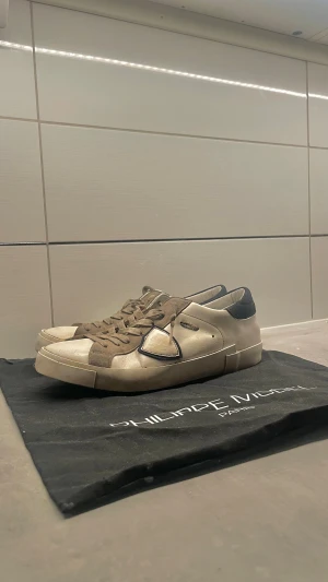 Philippe Model sneakers  - Snygga sneakers från Philippe Model i beige och vitt med svarta detaljer. Skorna har rund tå, platt sula och snörning. Ovandelen är i skinn med mockadetaljer och svart hälparti. Perfekt för dig som gillar stilrena och exklusiva sneakers.