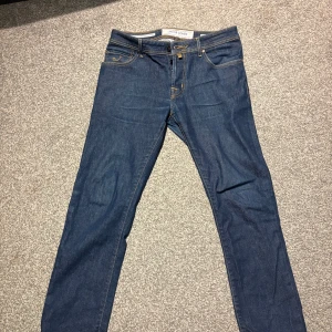 Jacob Cohen blå jeans Style 688 - Snygga blå jeans från Jacob Cohen, Style 688. Klassisk femficksmodell med gul kontrastsöm och broderad J på myntfickan. Jeansen har knappgylf och exklusiva detaljer på insidan. Perfekt för dig som gillar stilrena och kvalitativa jeans. Använda några gånger är i nyskick