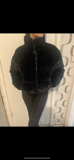 Svart pälsjacka från Nelly - Fluffig svart pälsjacka från Nelly med hög krage och dragkedja framtill. Jackan är kortare i modellen och har långa ärmar. Perfekt för dig som vill ha en mysig och trendig look under kyliga dagar.