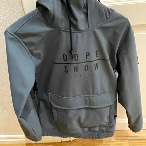 Grå hoodie från Dope Snow.   Storlek S - Säljer en grå hoodie från Dope Snow med stor magficka, huva med snörning och tryckt logga framtill. Perfekt för kalla dagar och snygg streetstil. Materialet känns slitstarkt och har en lite loose passform.