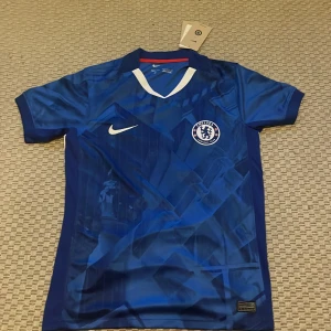 Chelsea FC Palmer 10 Nike matchtröja S - Chelsea FC hemmatröja från Nike i blått med Palmer 10-tryck på ryggen. Tröjan har korta ärmar, vit Nike-logga och Chelsea-märke på bröstet. Tillverkad i lätt och ventilerande material, perfekt för fotboll eller supporterliv.