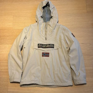 Beige skidjacka från Napapijri - Säljer en beige skidjacka från Napapijri med huva och halv dragkedja. Insidan är fodrad med mjuk fleece för extra komfort. Jackan är som ny och sparsamt använd. 