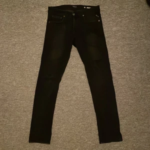 Svarta Replay Grover jeans W30 L32 - Svarta Replay Grover jeans med klassisk femficksdesign och slim passform. Helsvarta jeans, lite fade på låren. Inga defekter, köpta för 3 månader sedan. Pm för frågor och funderingar!