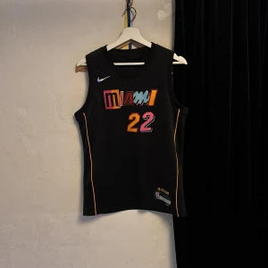 Miami heat basketjersey - Snygg svart miami heat-baskettröja från Nike med nummer 22 för Jimmy Butler.🏀 Färgglada detaljer i rosa, blått, gult och orange. Ärmlös modell i lätt och ventilerande Dri-FIT-material, perfekt för träning eller match. Passar runt S och är använd 2 gånger med ett strålande skick🤗Pris kan diskuteras vid snabb affär🤩🤩