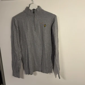 Grå half zip tröja Lyle & Scott - Snygg grå långärmad half zip tröja från Lyle & Scott. Tröjan är tillverkad i mjuk bomull och merinoull. Sparsamt använd utan defekter.