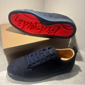 Christian Louboutin marinblå sneakers - Snygga marinblå sneakers från Christian Louboutin i mocka med klassisk röd sula och guldfärgad logga på insidan. Skorna har rund tå, snörning och en stilren design som sticker ut med den ikoniska röda undersidan.