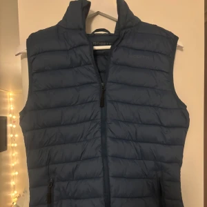 Blå dunväst från Rosetti Riding - Snygg blå dunväst från Rosetti Riding med quiltad design och hög krage. Västen har dragkedja framtill och två praktiska fickor med dragkedja. Perfekt för dig som gillar en sportig och stilren look.