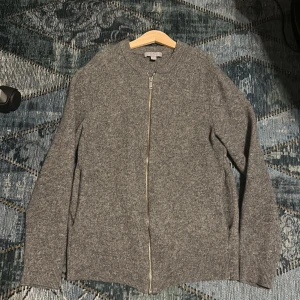 Grå cardigan med dragkedja från COS - Säljer den pga att den är för liten, Den är unisex och passar både tjejer och killar, Det står att det är storlek M men den passar nog bäst till XS eller under