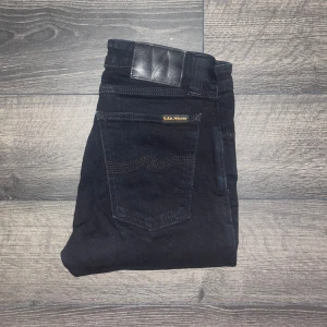 Nudie Jeans  - Svarta Nudie Jeans Skinny Sam med klassisk femficksdesign och smal passform. Tillverkade i 99% ekologisk bomull och 1% elastan för stretch. Snygga detaljer med svarta sömmar och diskret logga på bakfickan. JAG SKICKAR EJ FLER BILDER NÄR JAG BÄR JEANSEN! för storleksguide hänvisar jag till måtten och för bättre inblick i passformen rekommenderar jag att googla på modellnamnet. Jeansen kan vara uppsydda utan att jag noterat det så kolla måtten noggrant :) s3 midja 32cm, längd 100cm